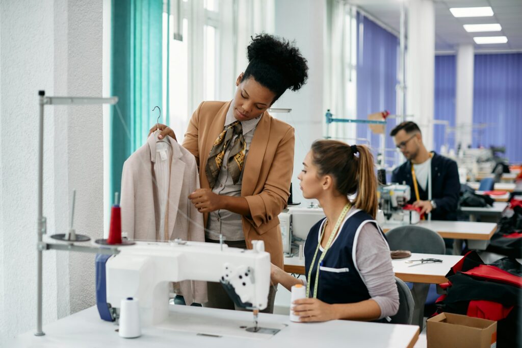 African American fashion designer giving instruction to a seamstress in a factory.