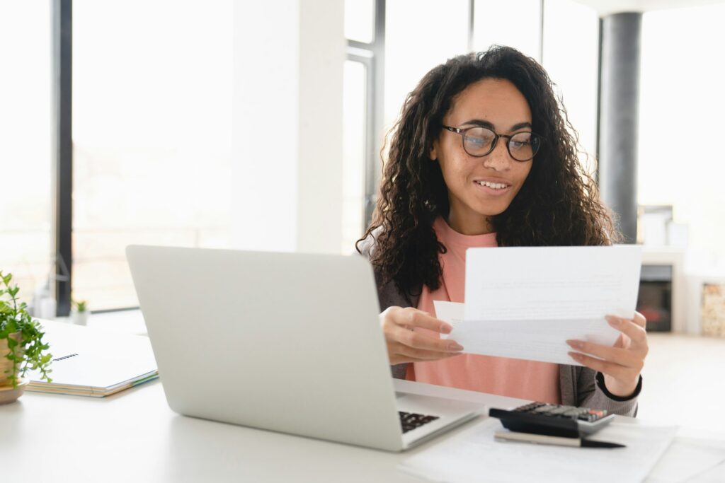 Happy african young housewife freelancer businesswoman counting paying domestic bills, e-banking